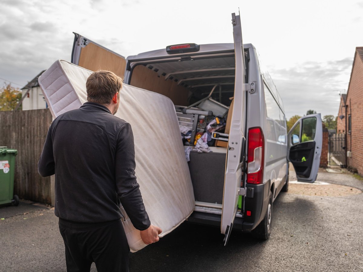 Man carrying and loading a mattress into a removal van outside a residential building during a house move. Concept of relocation, manual work and moving day activity.